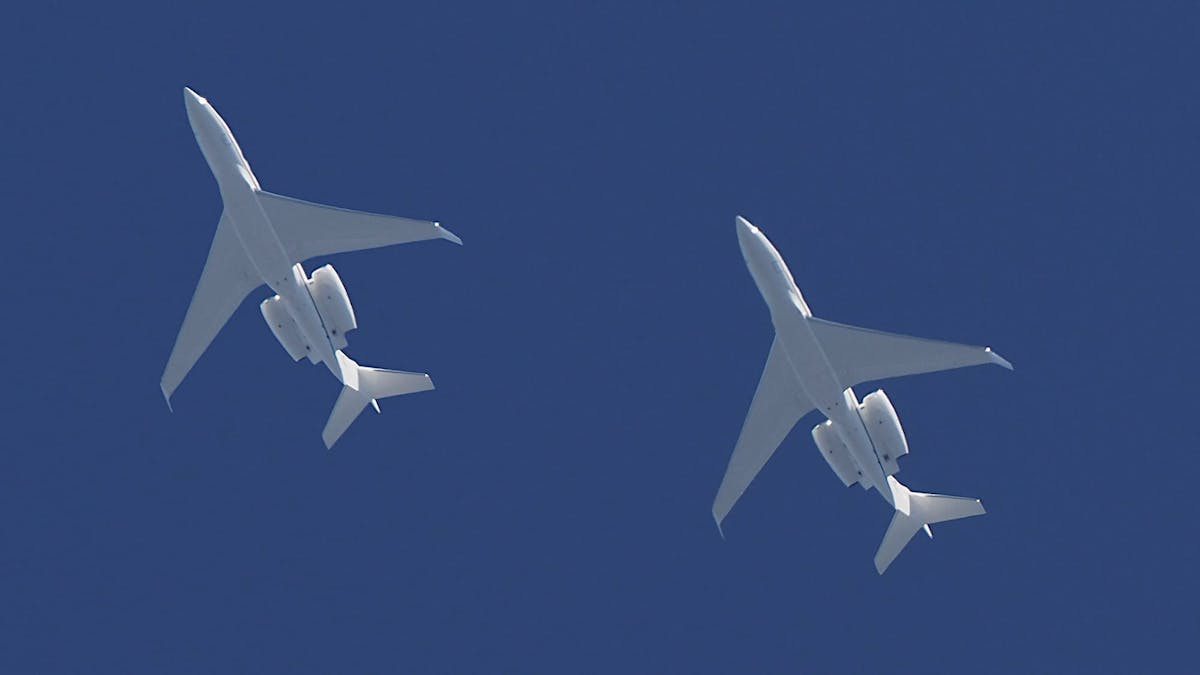 A shot from directly below 2 white large business jets.