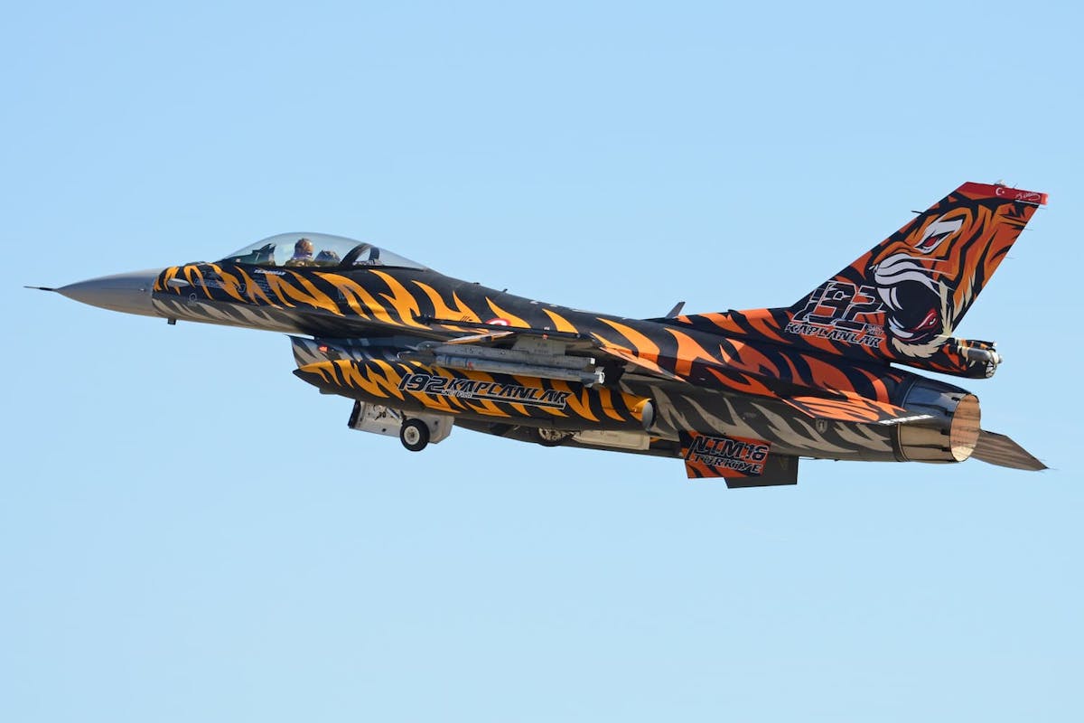 A Turkish F-16 with a tiger print livery flying through the sky.
